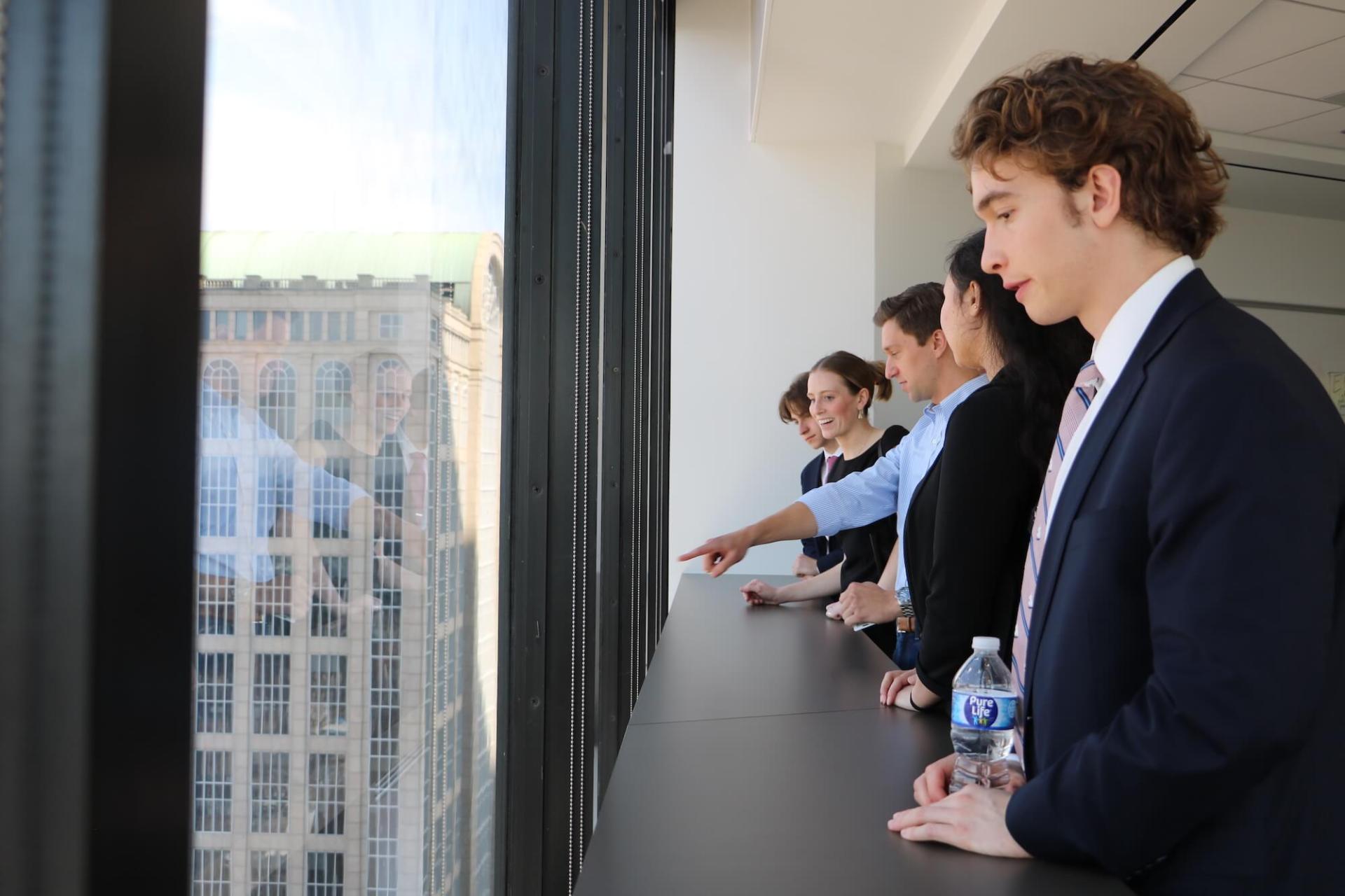 Accounting students look out the window of a Boston high-rise networking with alumni at a large accounting firm