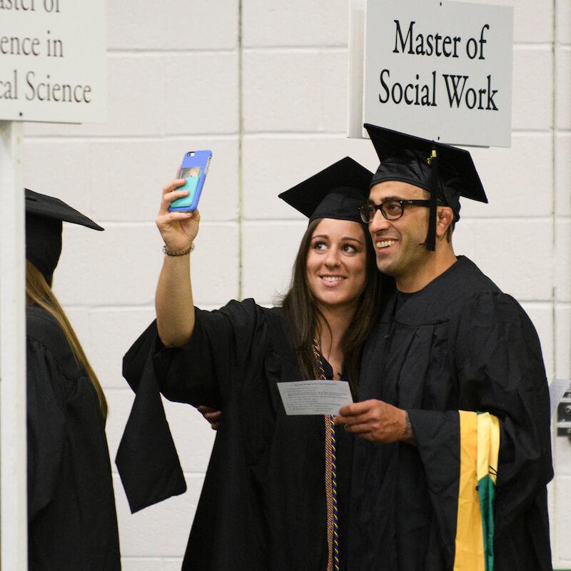 Smiling grads take selfies at commencement.