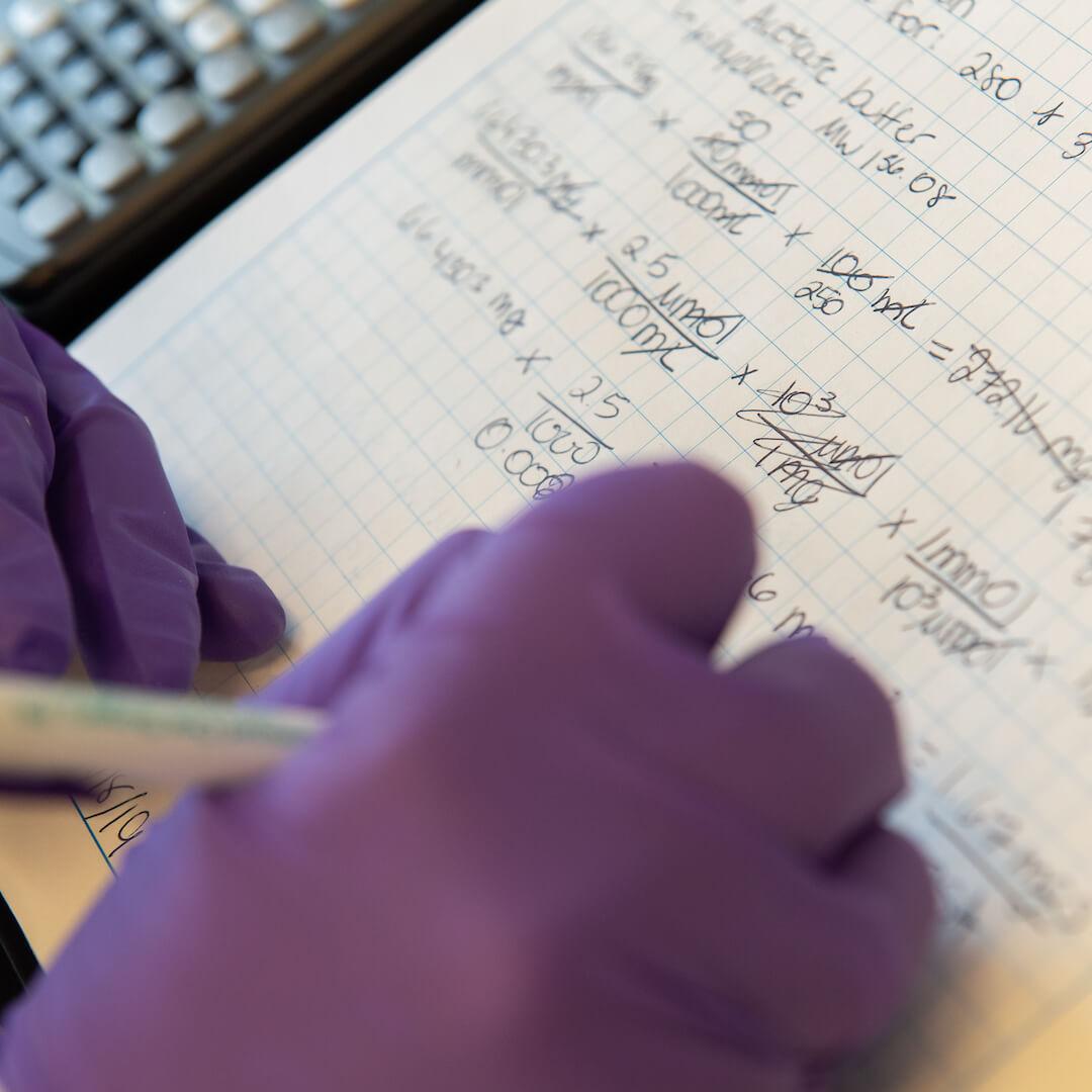 Writing down an equation while wearing purple lab gloves.