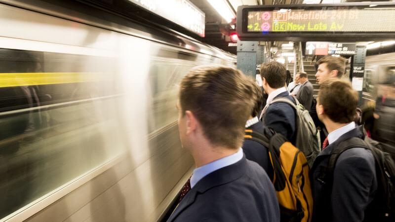 students stand on a subway platform as a subway zooms by