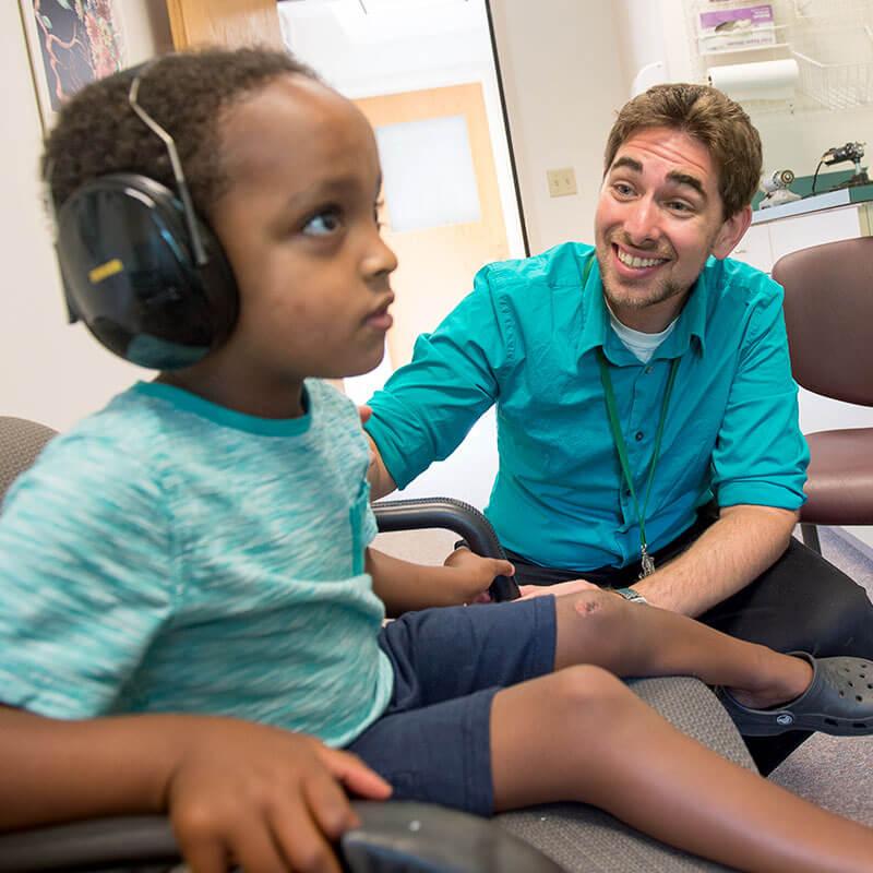 a child wears headphones while a person smiles at them