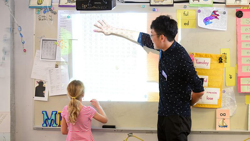 a student put his hand on a whiteboard while a child looks up at it