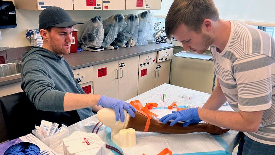 two students work on an appendage in a simulation lab