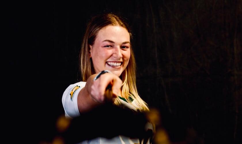 Taylor Mullen in her UVM Women's Lacrosse jersey holding across stick forward and smiling.