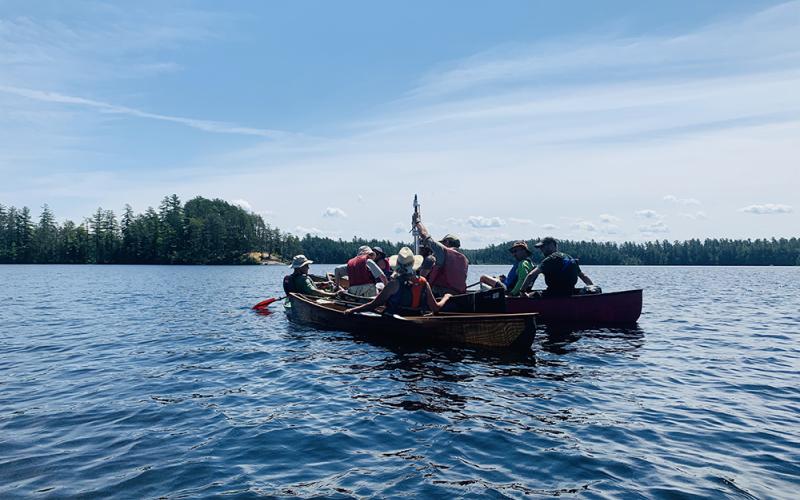 Tour participants looks at a sediment core pulled up from the lake. A canoeist holds up a sediment core that they pulled up from the lake bottom.