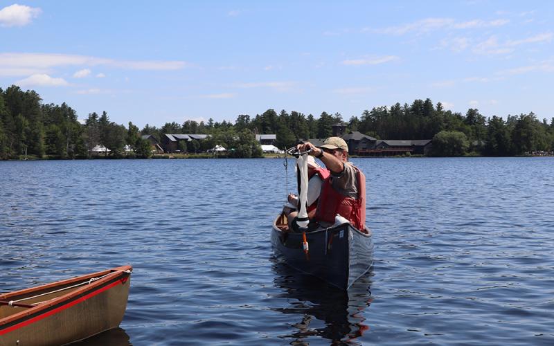 Dr. Stager holds a plankton tow. A man in a canoe holds up a plankton tow that he just pulled from the water.