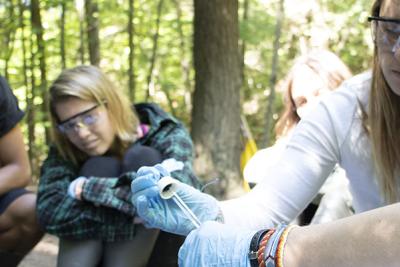 Students wearing safety goggles learn from instructor in a wooded setting