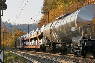 Train with tanker car on tracks with forest on either side