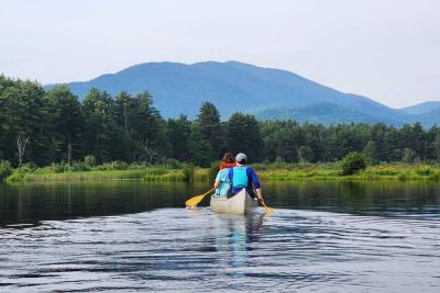 Photo of fellows in canoe paddling toward mountain.