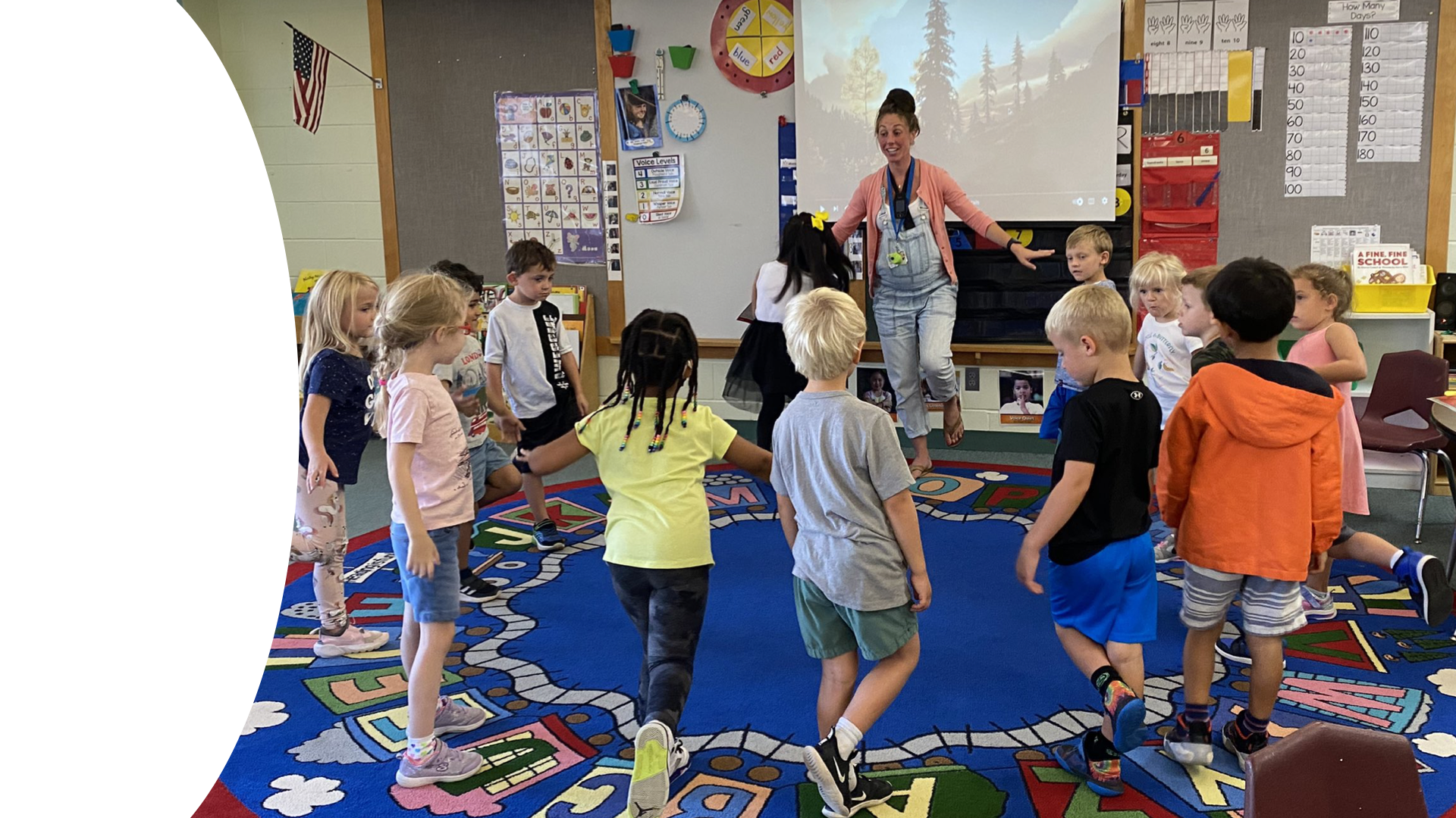 An educator in a messy bun and overalls leads a circle of students in a stretching exercise in a cozy classroom