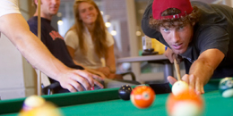 A student lines up a shot in a game of pool while another student watches