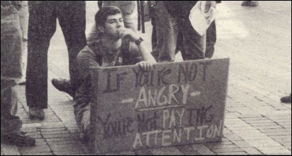 [Protestor With Sign Which Reads If Your Not Angry You're Not Paying Attention]