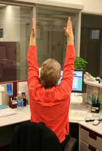 woman at desk with arms extended over head