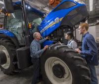 Young farmers receive training from an instructor while standing next to a tractor.