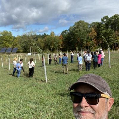 Picture of a man with sunglasses and brown hat with a group of people in the background.