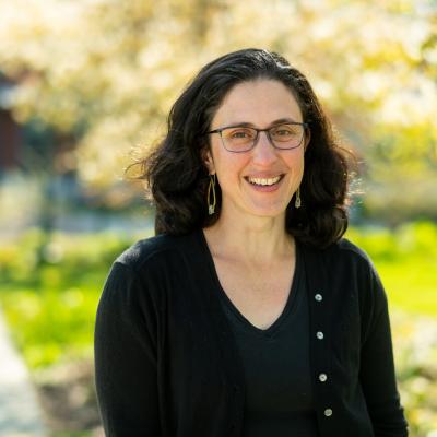 In this portrait of Rachel Schattman, she is standing outside, smiling at the camera. 