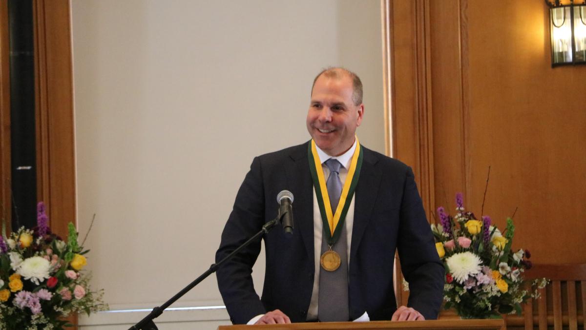 Professor Brewer wearing medal and standing at podium, smiling