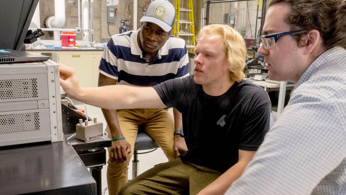 Research Assistant Professor Jackson Anderson provides senior Electrical Engineering students Couby Ouattara and Tom Sykes an introduction to the wafer prober station