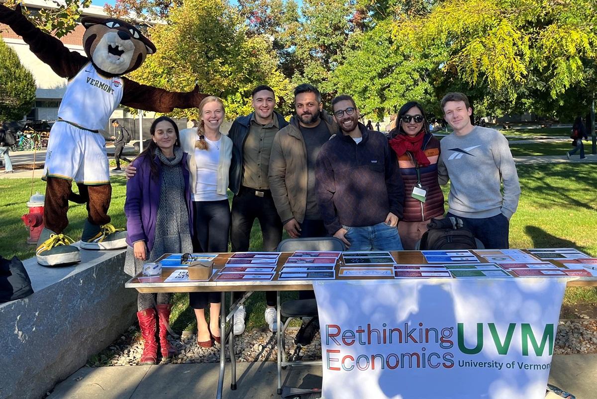 A group of students and the mascot Rally Cat at a club table outside on UVM's campus with a 