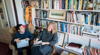 Two people sitting in chairs in front of a large bookcase. 