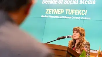 a person speaks at a podium while an audience member looks on