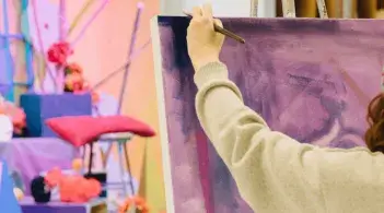 Student painting a blue, purple and pink still-life