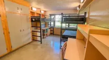 Residence hall room with three beds, two closets, a dresser, and three desks. 