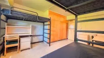 A room with three beds, three desks, a dresser, and two built-in closets. 