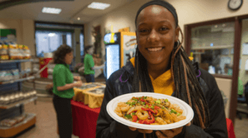 Student in dining hall holding a plate of stir fried shrimp