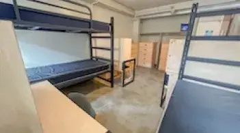 A room with three beds, three dressers, and three desks. 