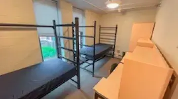 A room with two beds, two desks, and two dressers. 