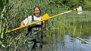 Olivia wades into the lake holding a sample collector