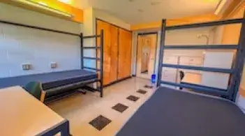 A room with two beds, two built-in closets, two desks, and tile floors.