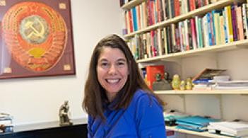 A person sitting at a desk, surrounded by a bookshelf filled with books.