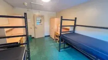 A room with two beds, two dressers, and two desks. 