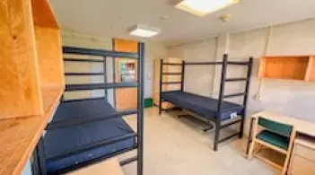 A room with two beds, two dressers, and two desks. 