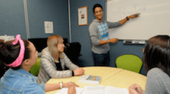 tutor standing at white board, students sitting at table watching tutor