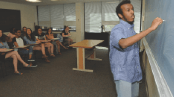 tutor writing on blackbaord, students sitting and watching