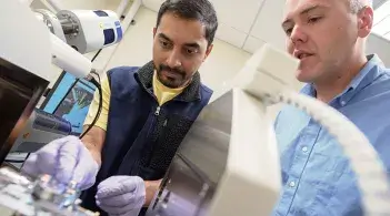 A graduate students works with Professor Matthew White on the electron microscope