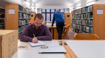A person sitting in the library writing in a notebook