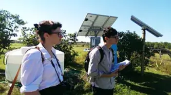 Two individuals standing in front of a solar panel taking notes
