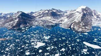 Grey mountains with snow on them. Dark blue ice is in the foreground.