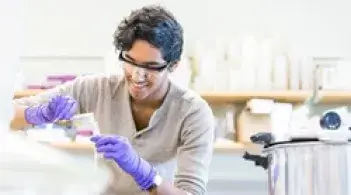 Student in a lab wearing goggles and gloves pouring liquid