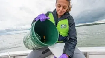A student sitting on a boat on the lake pouring water from a 5 gallon bucket into a funnel