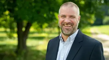Photo of male faculty member smiling and standing outside in front of a tree.