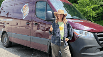 Photo of woman holding a thumbs up standing in front of a large red van.