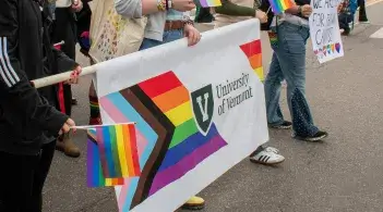 Students march with the UVM Pride banner, displaying the progress pride flag with the UVM logo in the center.