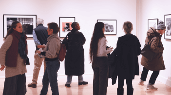Many people fill the east galley, looking closely at the artwork on display.