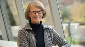 Sue Dinitz, long-term director of the UVM Writing Center, poses in front of windows on an autumn day.