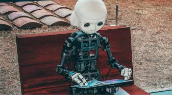 A humanoid robot reads a book while sitting on a park bench.